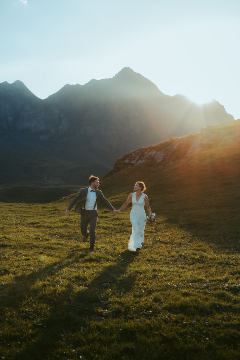 The evening of their elopement, a couple runs through a field during golden hour