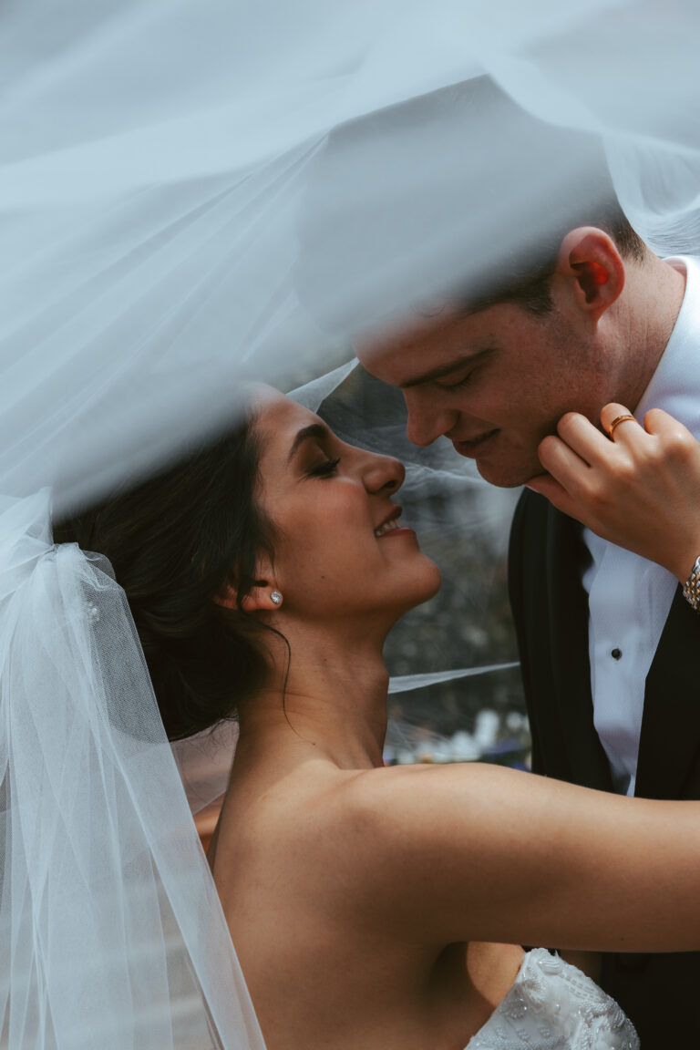 A bride and groom stand under the bride's veil, about to kiss