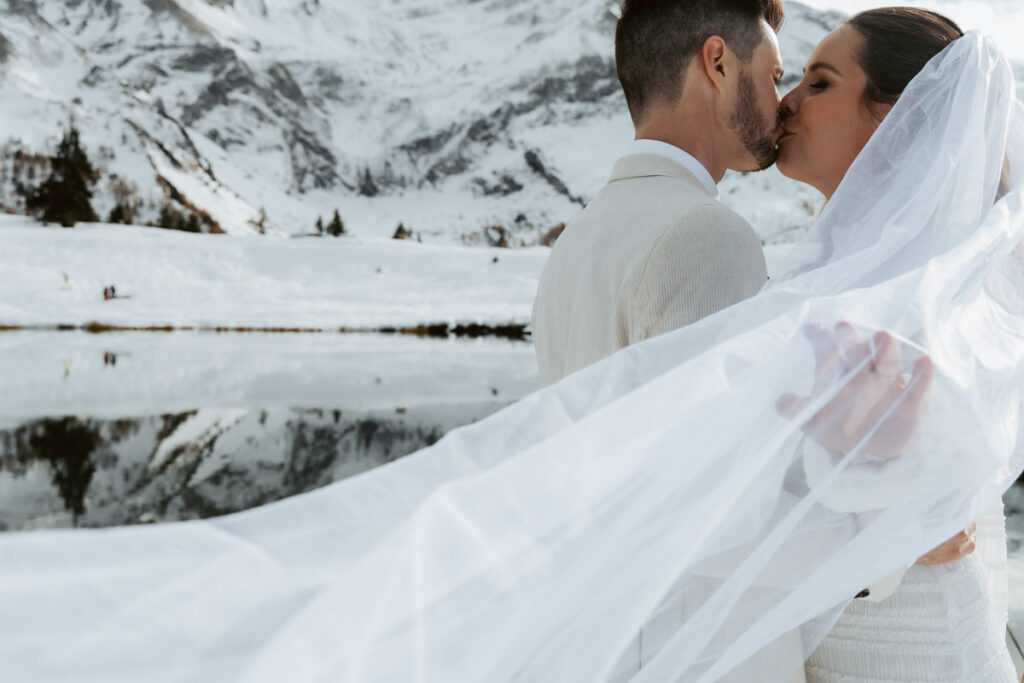 A couple kisses as the wind blows the bride's veil in the air during their winter elopement in Switzerland