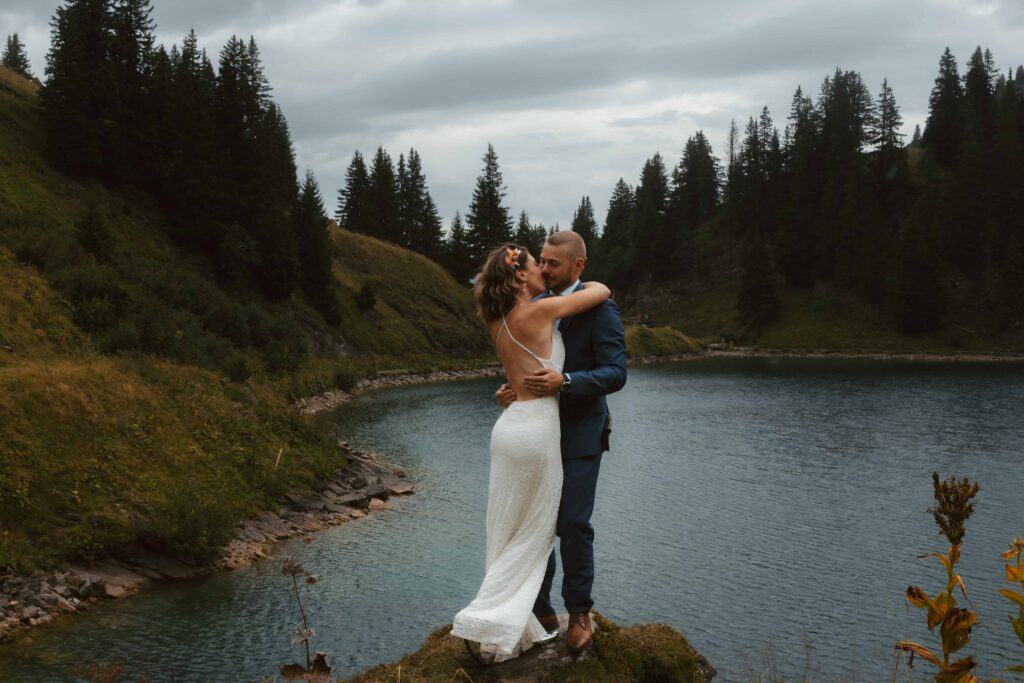 A couple holds each other close in the rain in front of an alpine lake and pine trees during their Swiss elopement