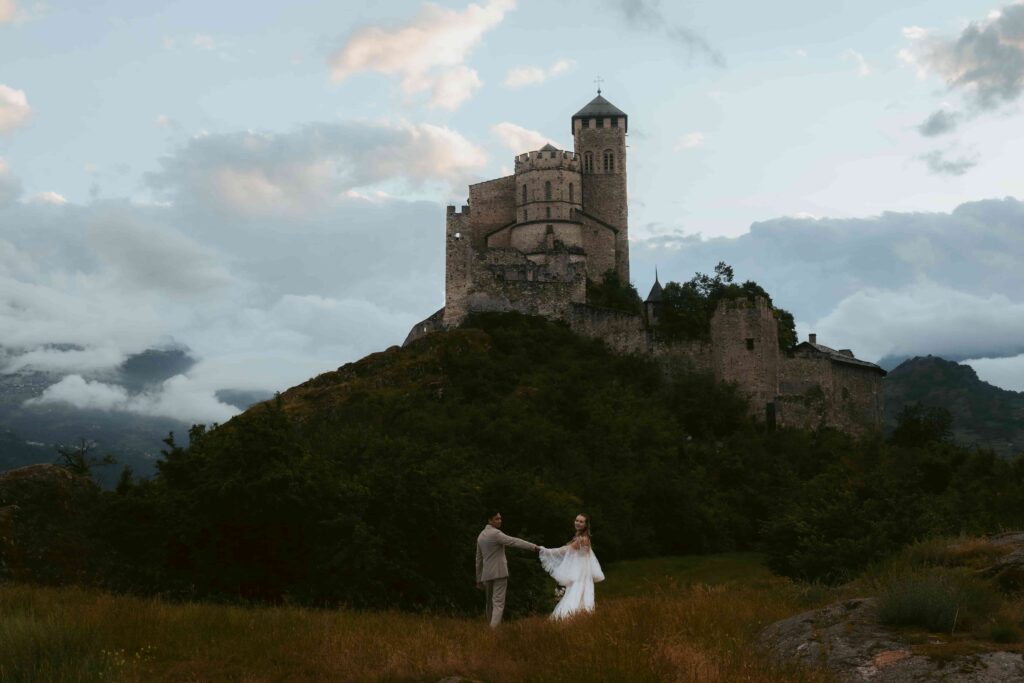 A couple walks in a meadow in front of a castle during their elopement