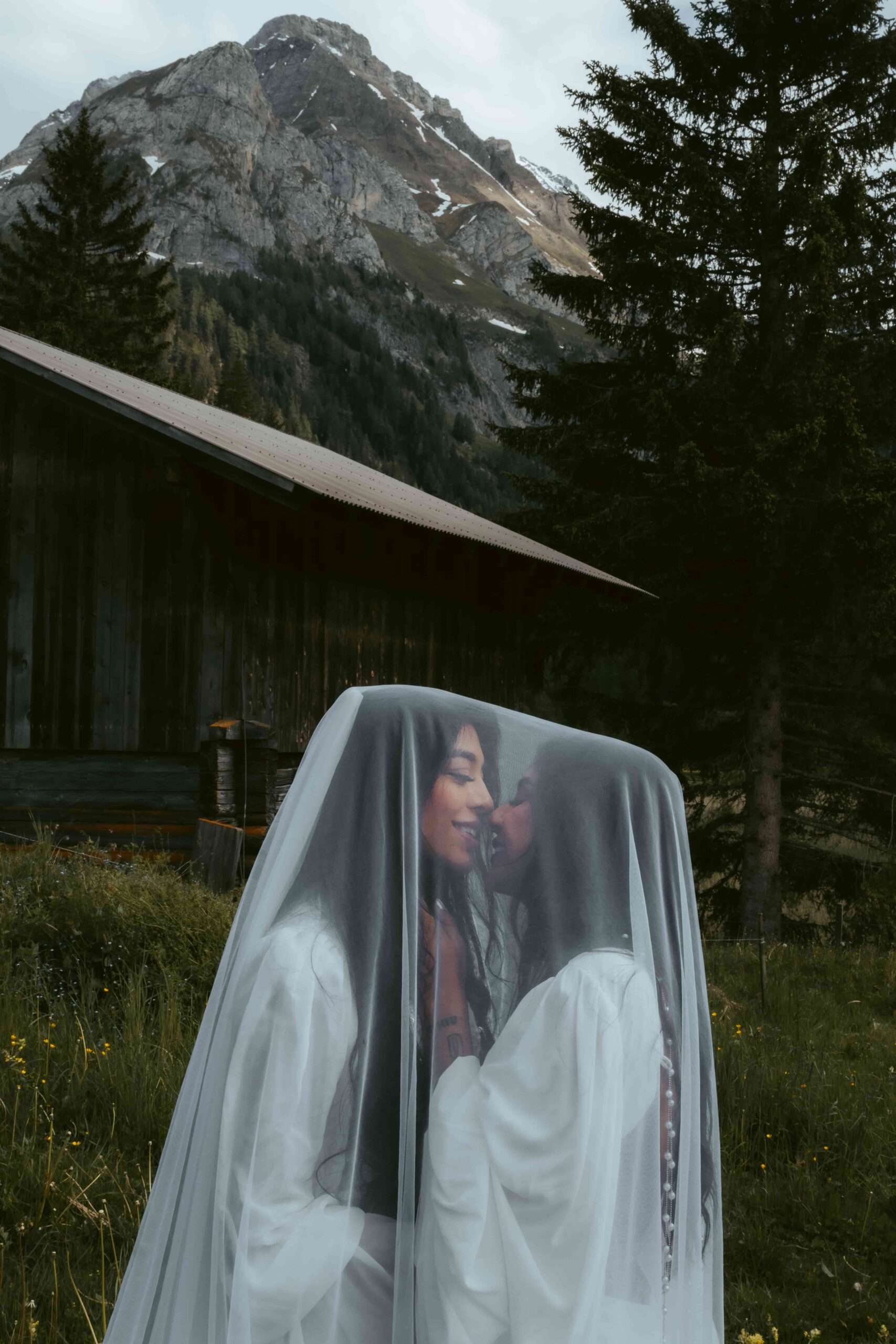 Two women kiss in fron of a mountain hut and the alps during their Swiss elopement