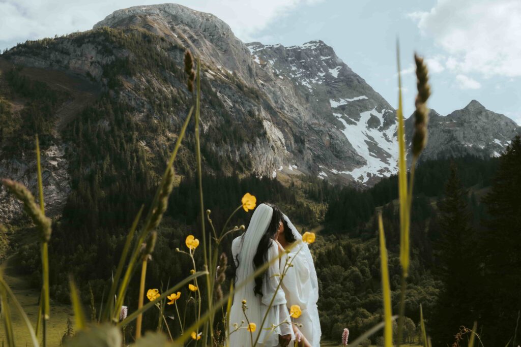 A couple looks fondly at each other while standing in a meadow in front of the alps during their intimate wedding