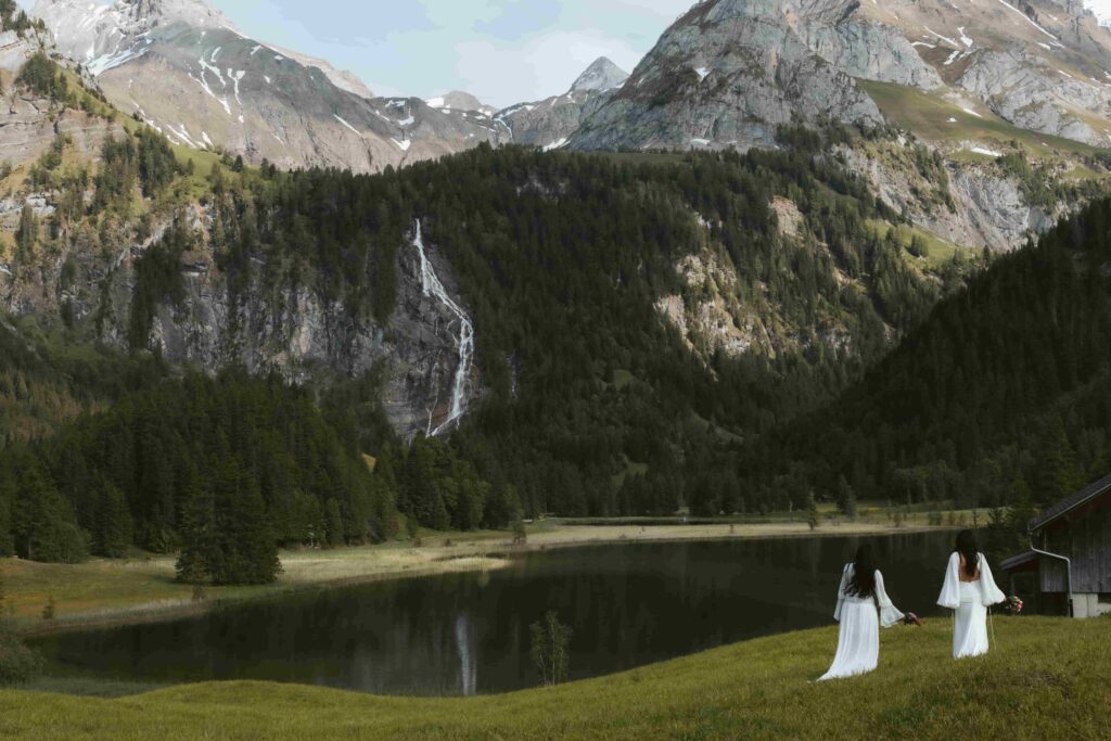 Two women face a waterfall and a lake in summer during their elopement